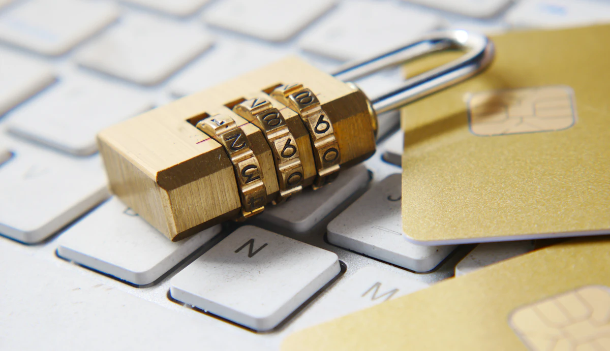 A brass combination padlock resting on a white computer keyboard alongside gold payment cards